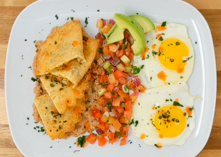 breakfast plate on a wood surface with empanadas, pico de gallo salsa, avocado and eggs with hot sauce