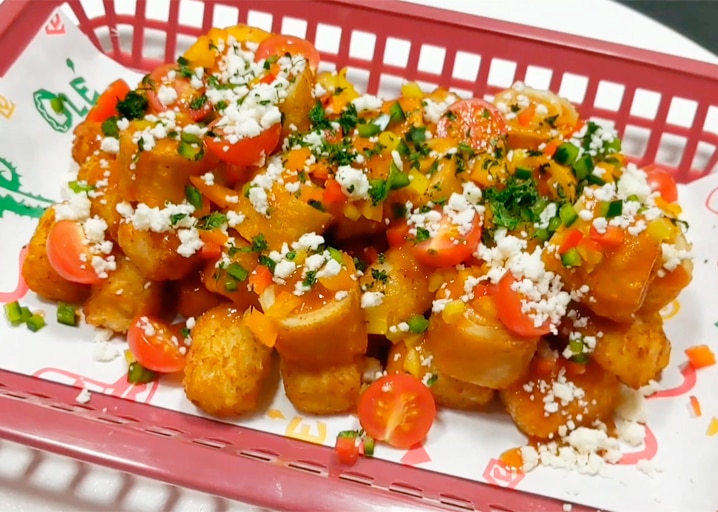 plastic basket filled with tater tots made from tornados taquitos with tomatoes, peppers, cheese and cilantro