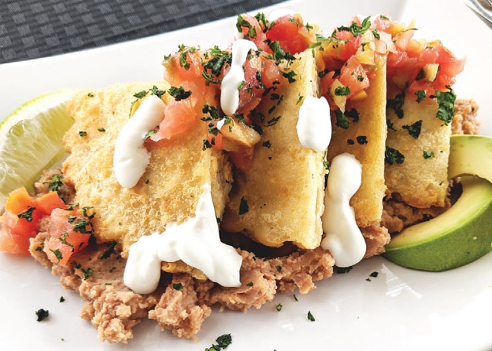 plate with empanadas cut open on top of refried beans, topped with pico de gallo salsa, cilantro and sour cream with avocado and lime on the side