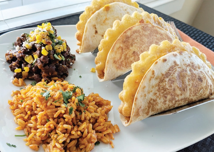 plate with empanadas wrapped in tortilla in taco holder with black beans and rice on the side