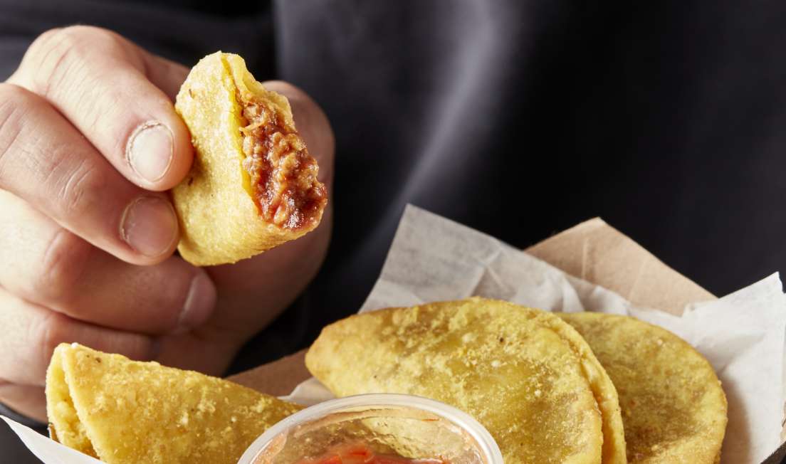 Mini tacos in a paper boat with salsa being picked up by a person in a dark shirt