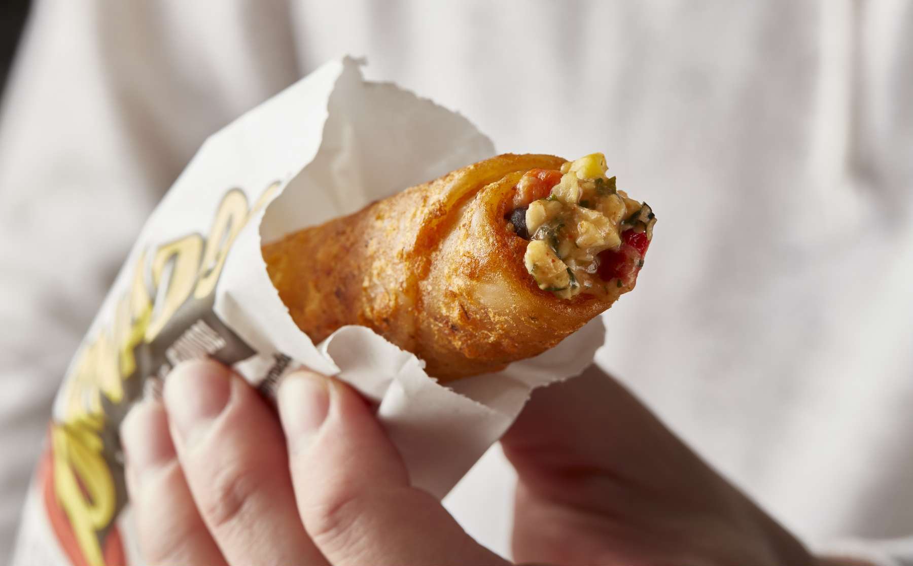 hand holding a Tornados taquito filled with chicken, corn and sauce in a serving sleeve