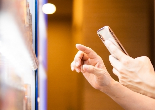 A person reaching to touch a vending machine with a phone in their other hand