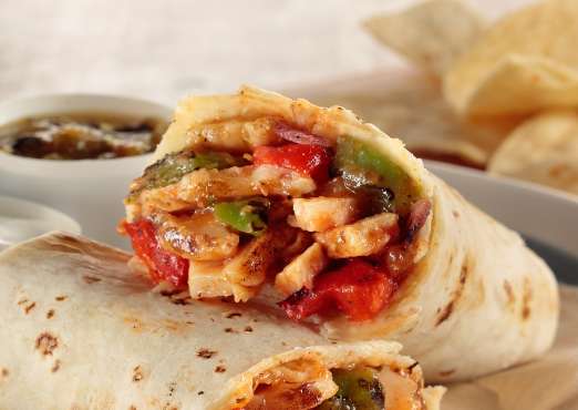 burrito cut open showing grilled chicken, peppers and chips and salsa in the background