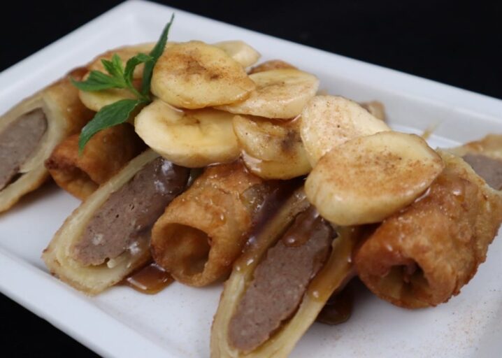 Three French Toast & Sausage Sliced Down The Middle, Plated And Topped With Bananas, Cinnamon And Syrup