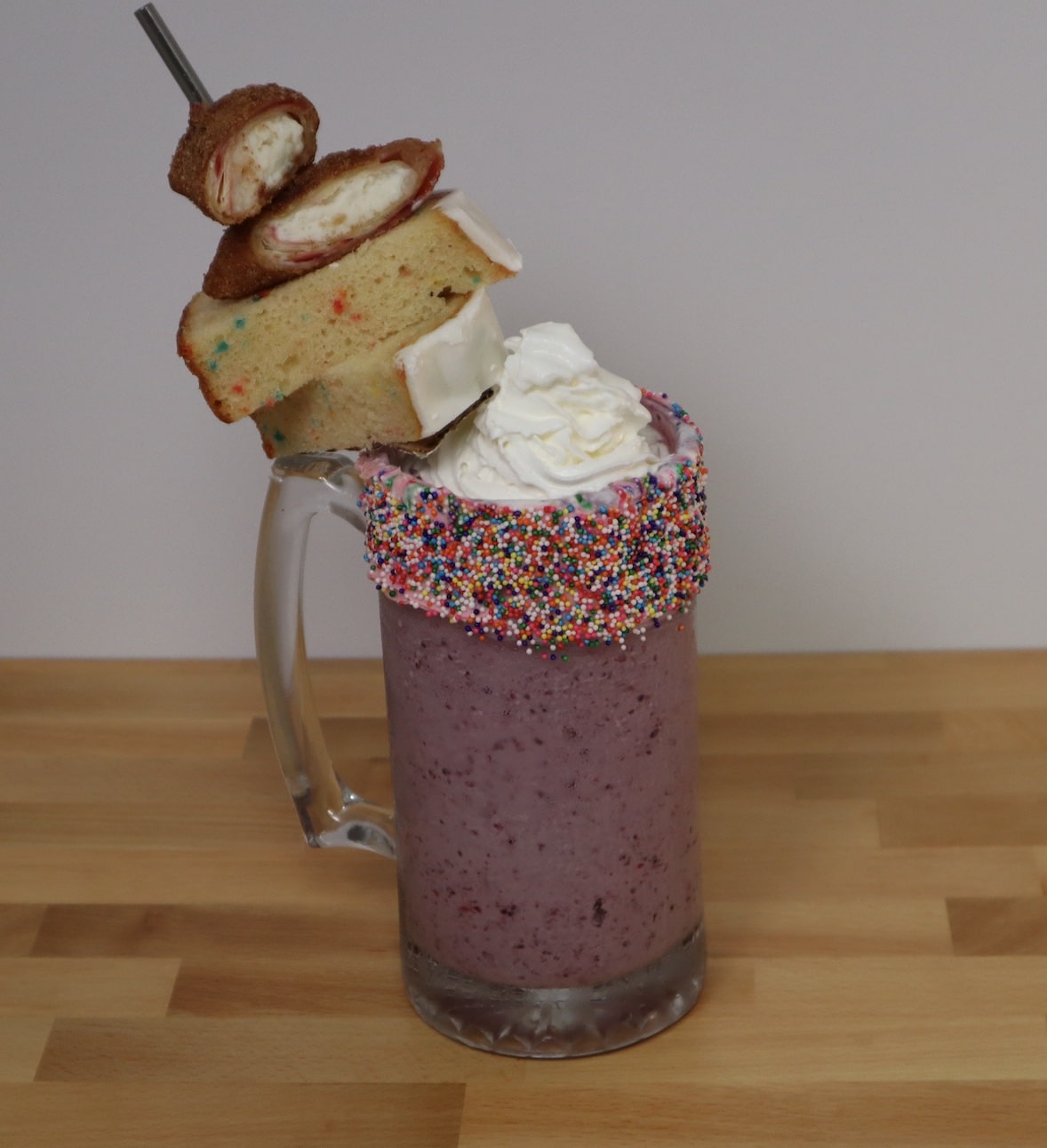 Mixed berry shake in a glass mug, topped with sprinkles, whipped creme, fruit loaf and raspberry cheescake mini chimi