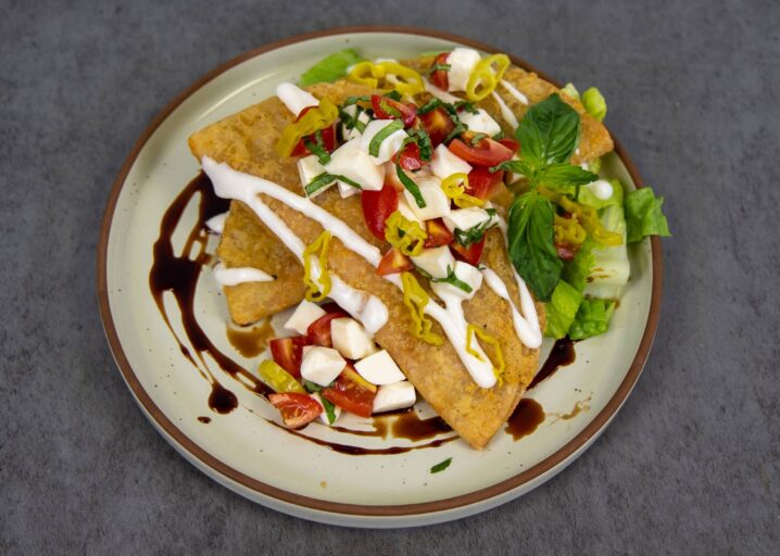 Cheesy Pepperoni Panadas Plated And Topped With Tomatoes, Cheese, Sour Cream, Basil And Peppers