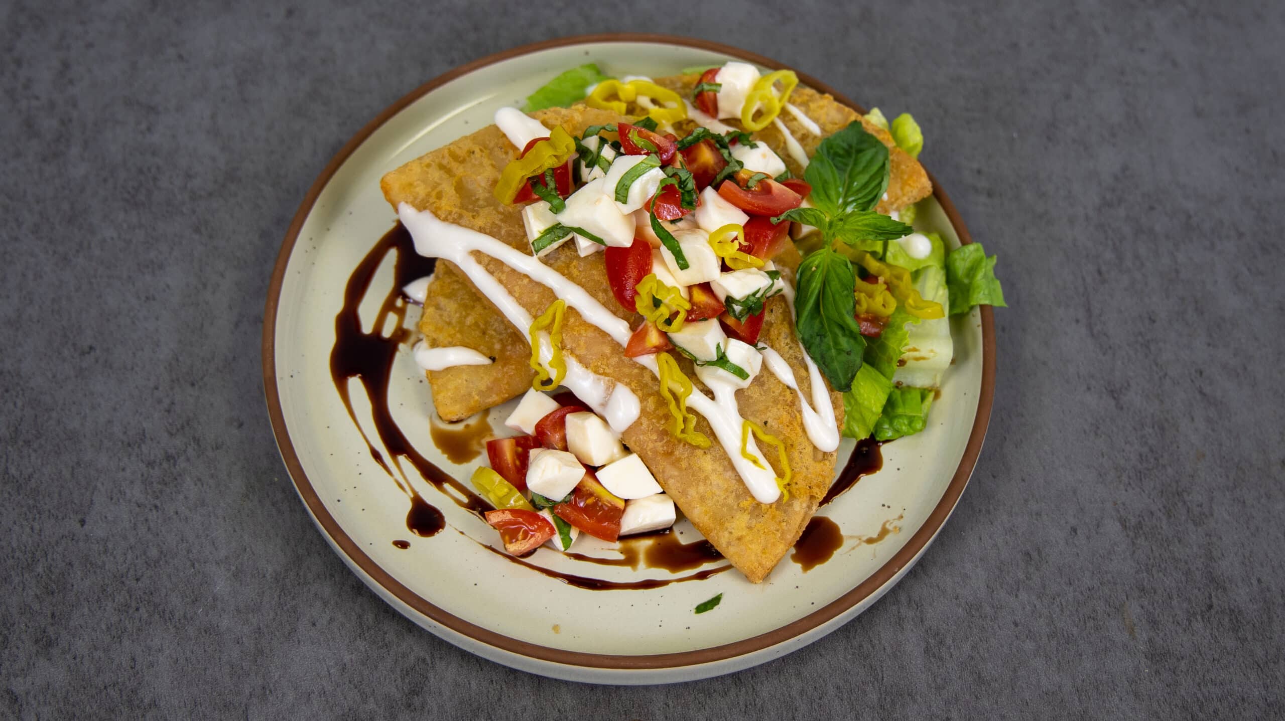 Cheesy Pepperoni Panadas plated and topped with tomatoes, cheese, sour cream, basil and peppers