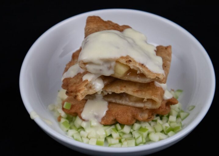 Two Apple PIe Empanada Slice And Plated On Top Of Diced Granny Smith Apples, Drizzled With Creme Anglaise