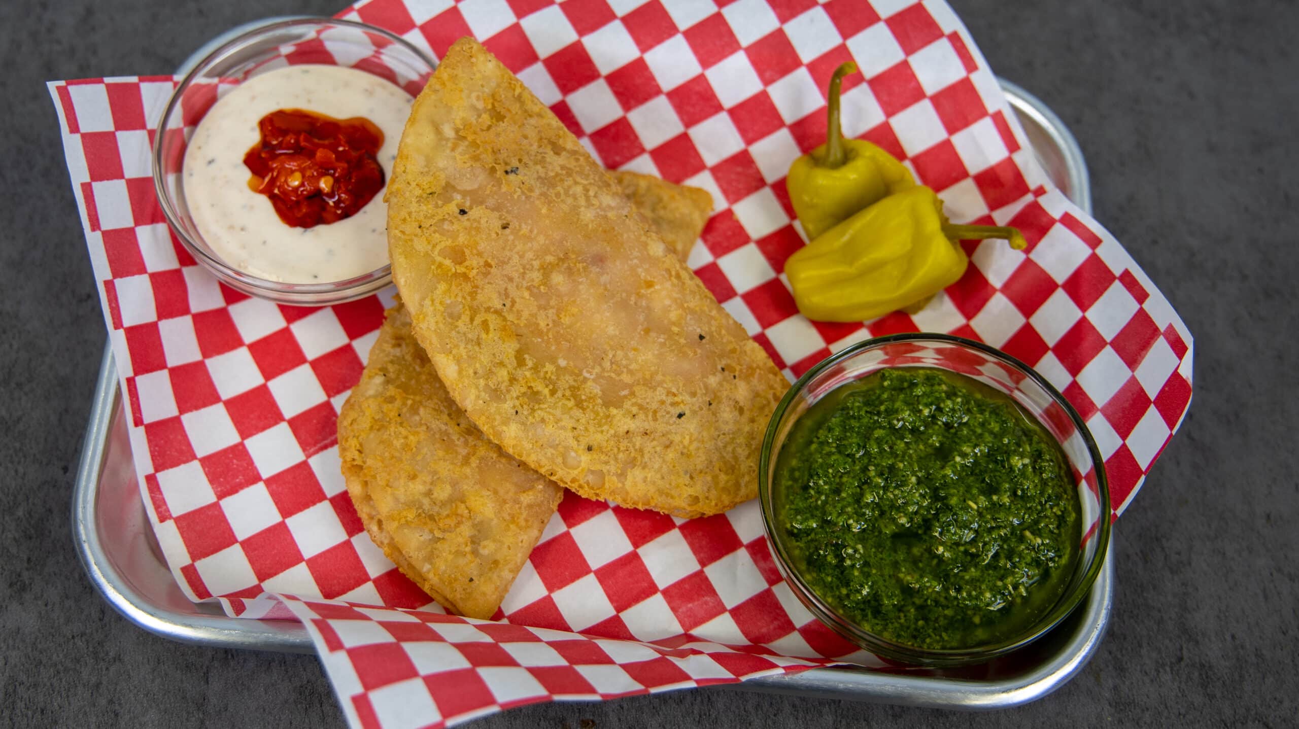 Cheesy Pepperoni Panadas plated on a metal tray with paper lining served with pesto, a dipping sauce and peppers