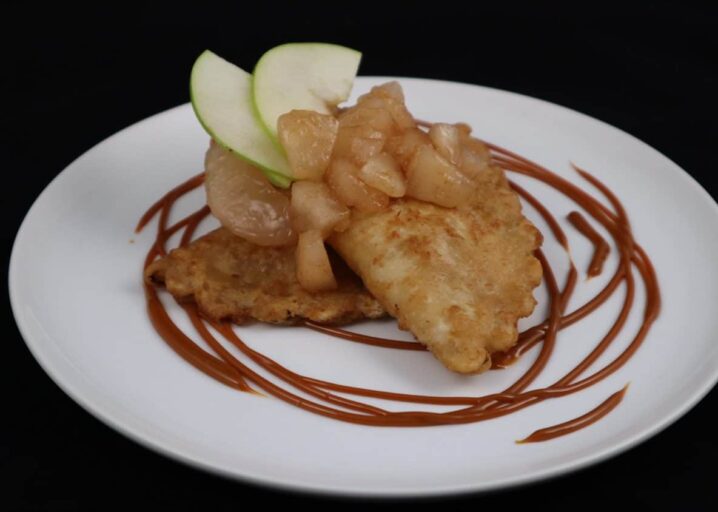 Two Apple Pie Empanada Plated And Topped With Diced Granny Smith Apples And Garnished With A Caramel Drizzle