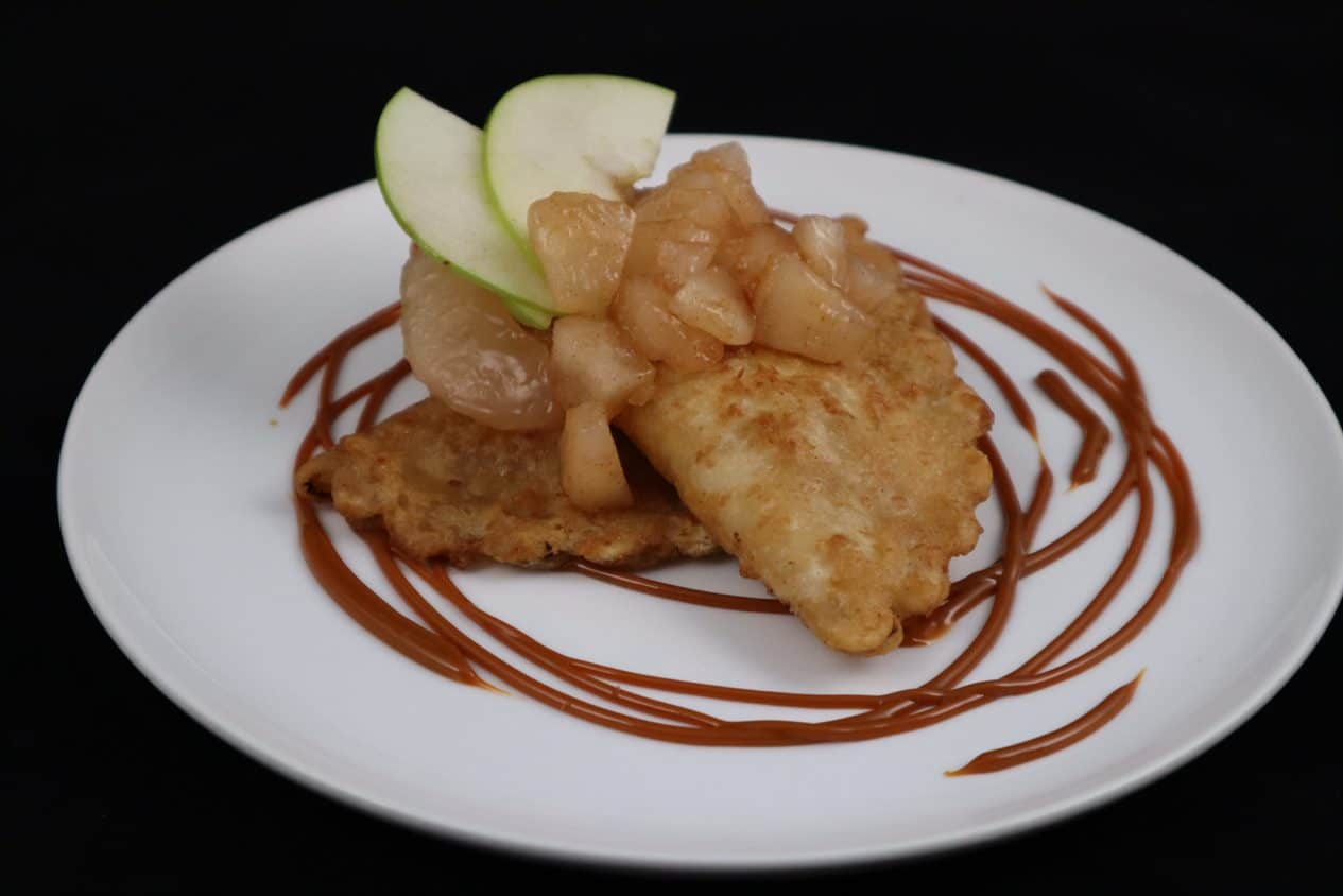 Two Apple Pie Empanada plated and topped with diced granny smith apples and garnished with a caramel drizzle