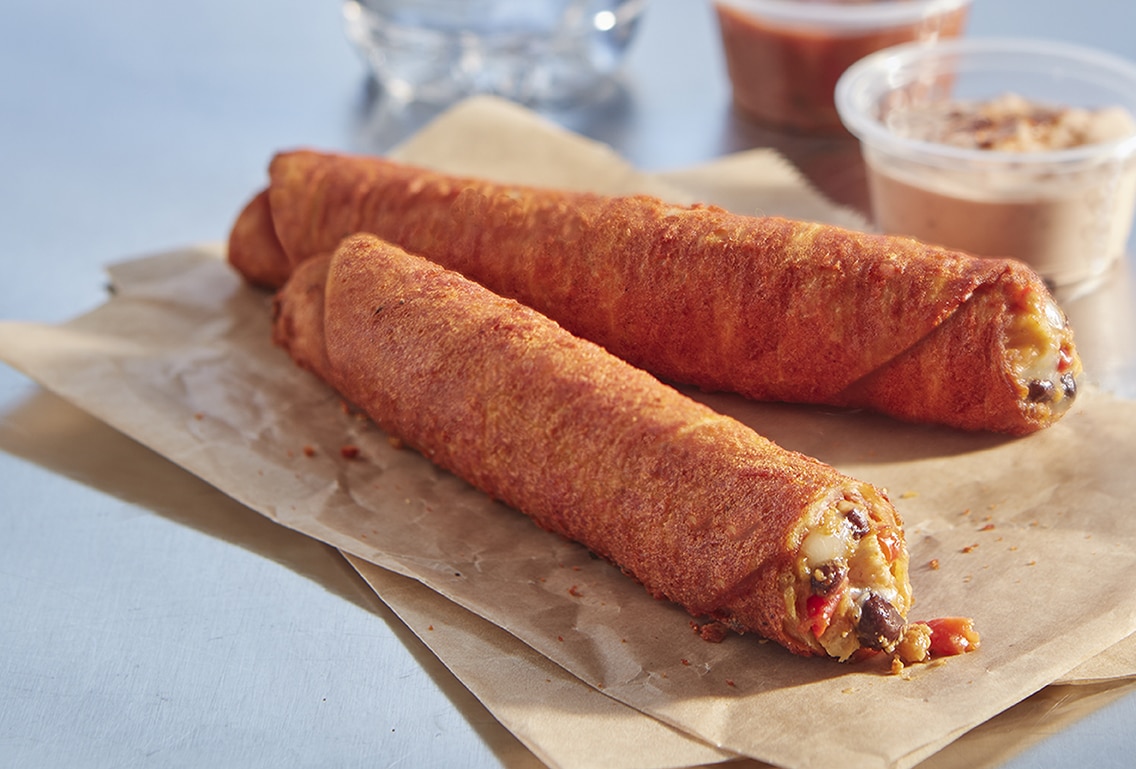 Two Spicy Chipotle Chicken Tornados on a napkin next to a small plastic container of dipping sauce
