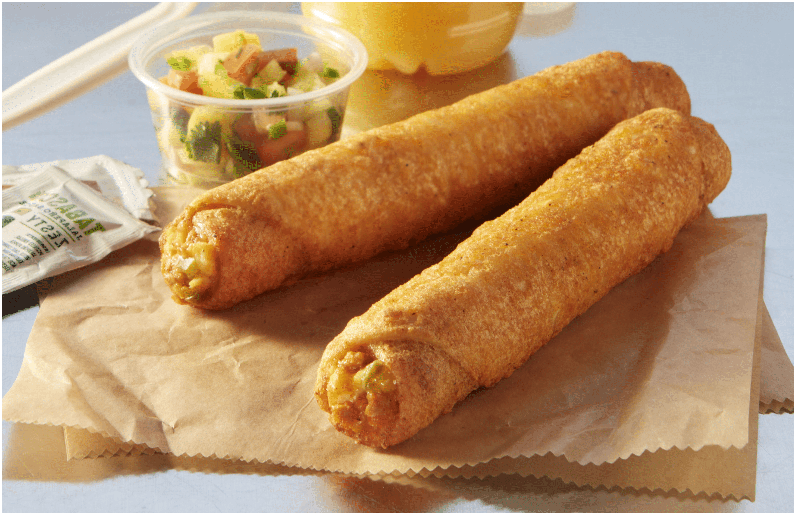 Two Cheesy Breakfast Chorizo Tornados on a napkin next to a plastic dish of salsa