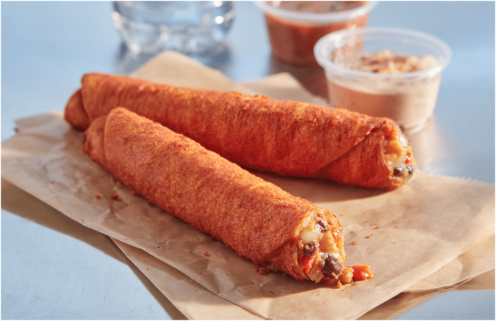 Two Spicy Chipotle Chicken Tornados on a napkin next to a plastic dish of queso