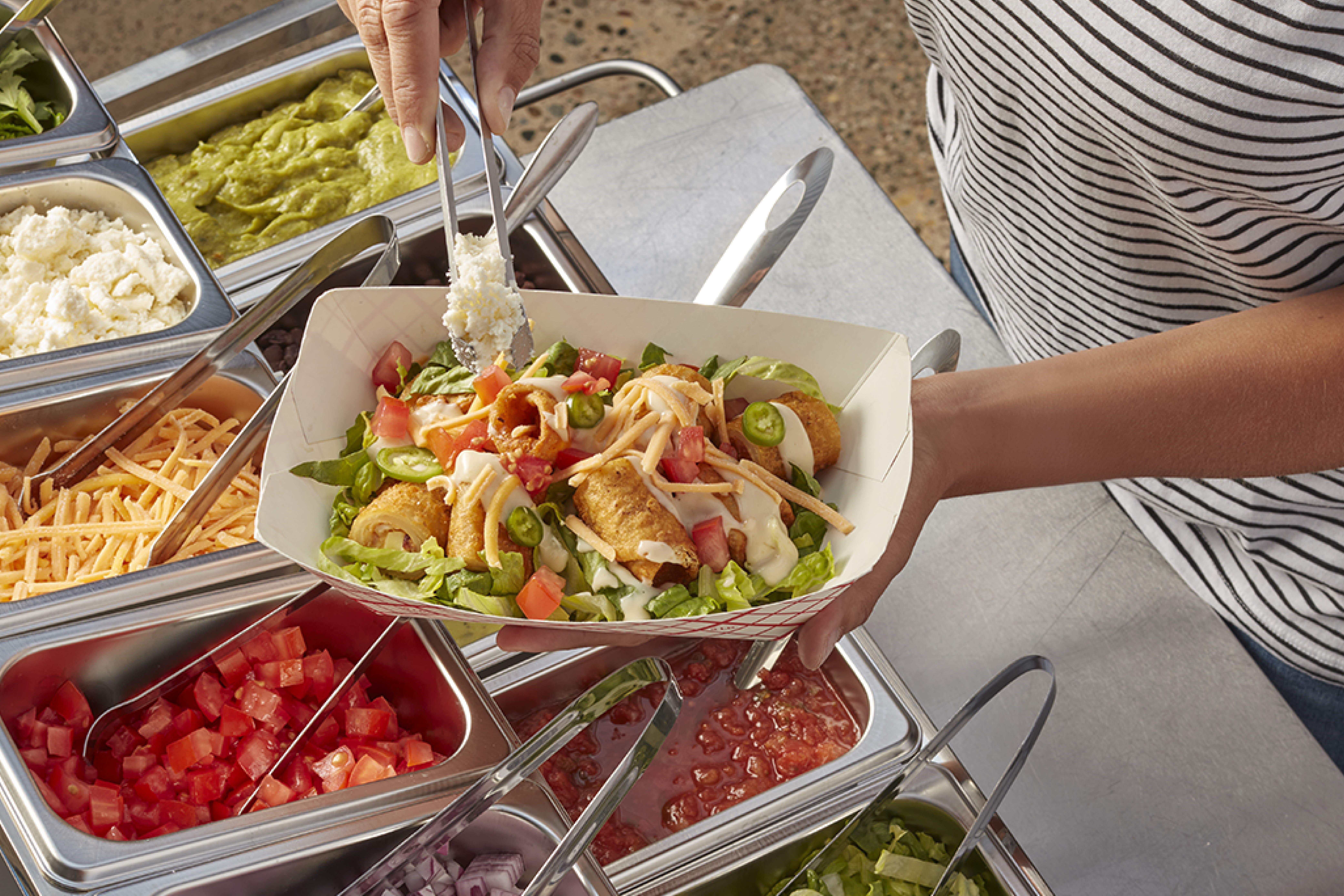 Topping a paper boat filled with chopped Tornados and greens with other condiments