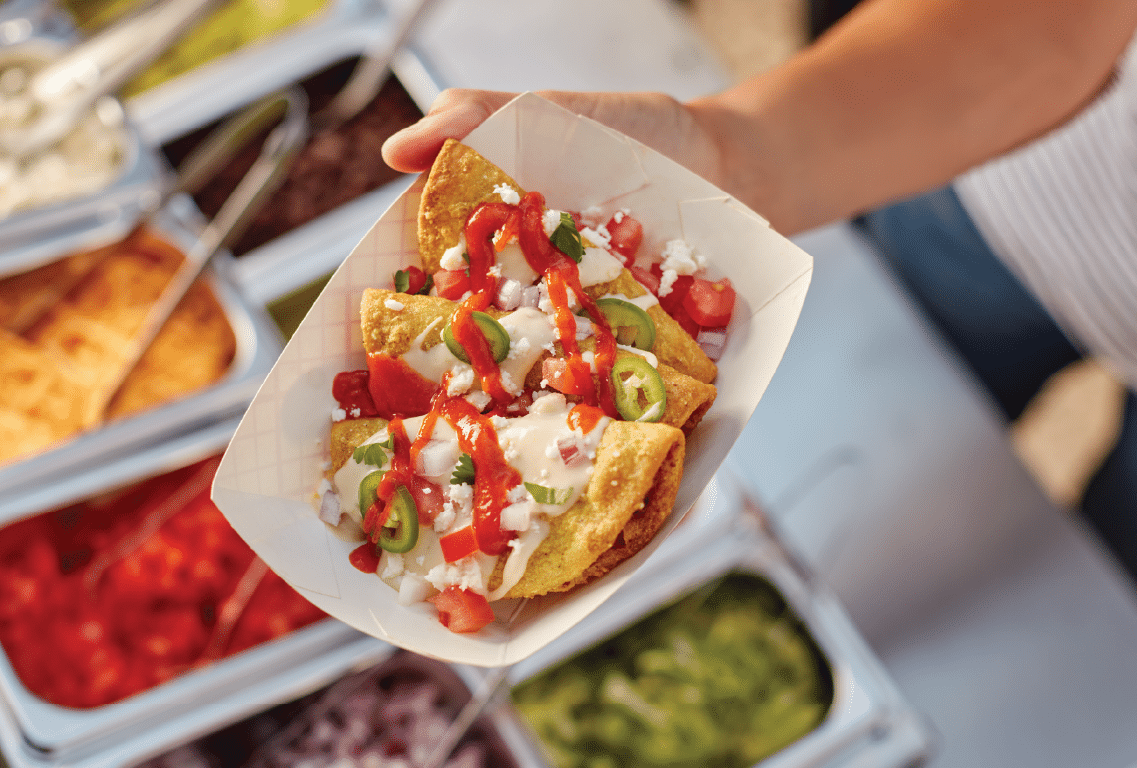 Mini Tacos in a paper serving boat, topped with queso, hot sauce and jalapeños