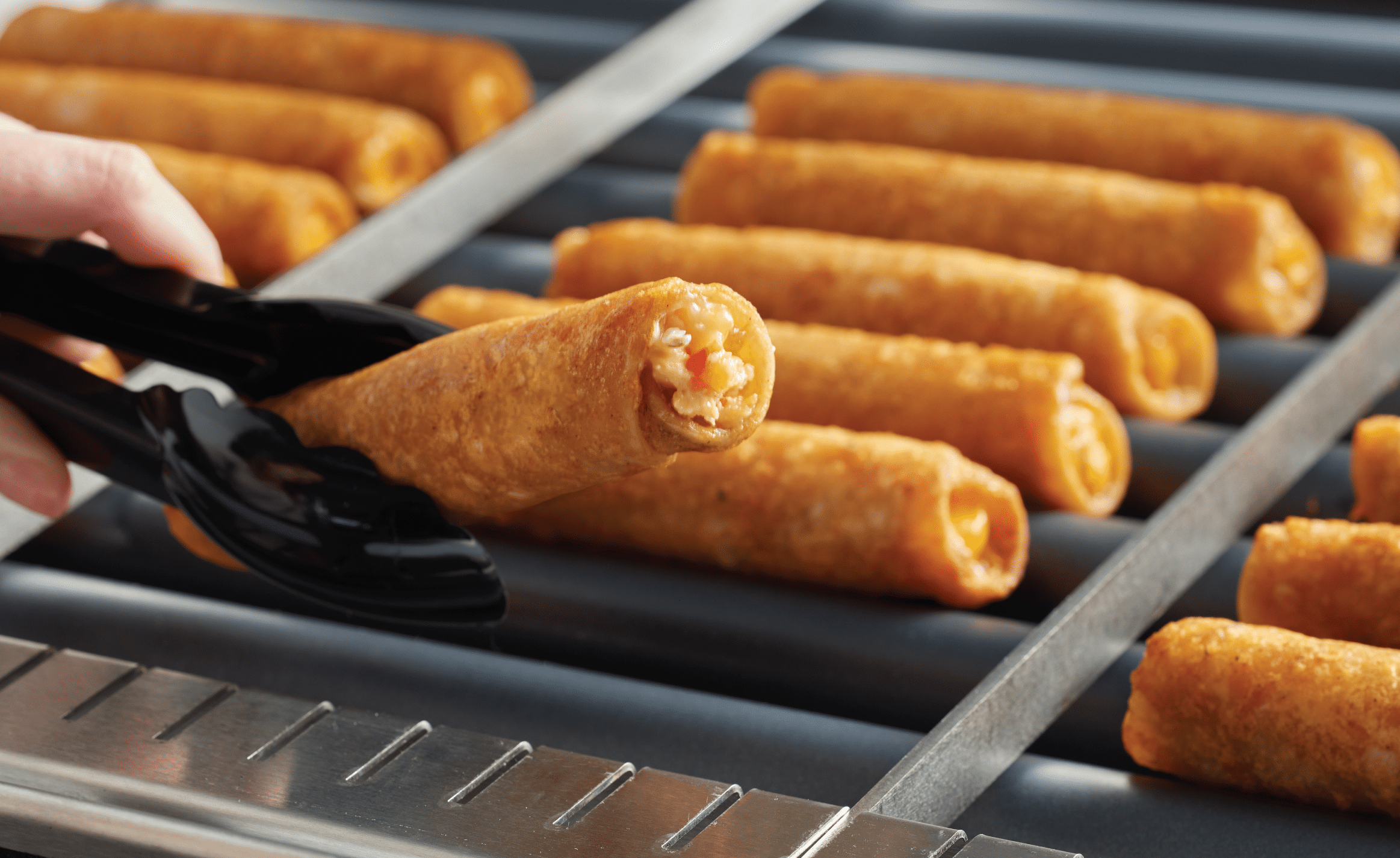 Tongs picking up a taquito off a roller grill